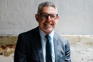 Bespectacled man with greying cropped hair and wearing suit and tie