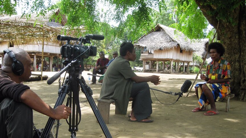 Journalist Scott Waide sits on the ground as a female journalist is interviewing another woman in PNG.