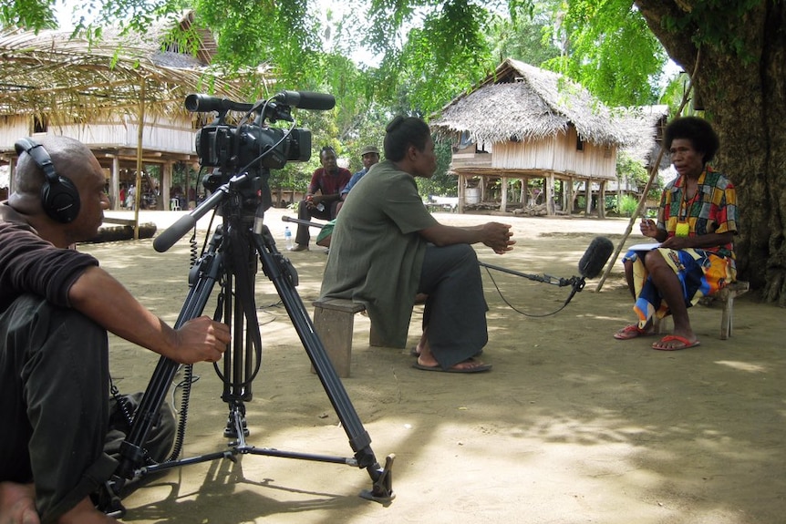 Journalist Scott Waide sits on the ground as a female journalist is interviewing another woman in PNG.
