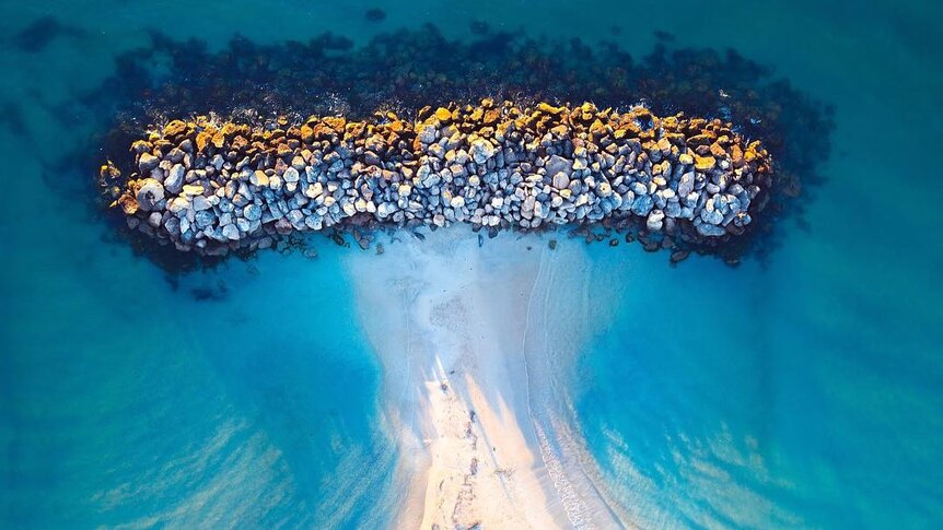An aerial photo of a stone retaining wall in the ocean.