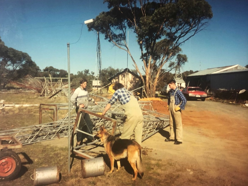 A man and two older boys building a radio tower while the family dog looks on