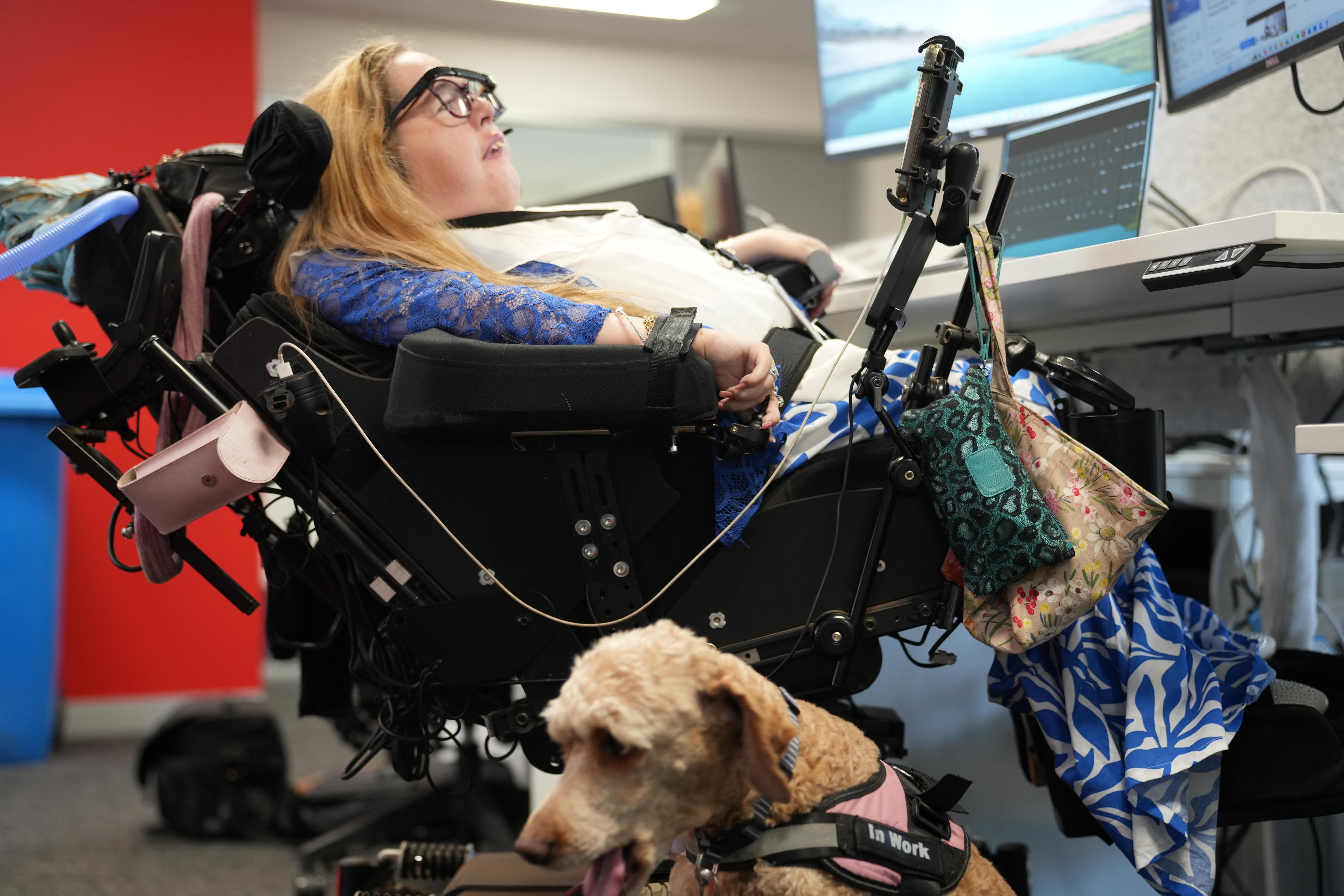 A woman in a wheelchair with a dog with her feet heard, at an office.