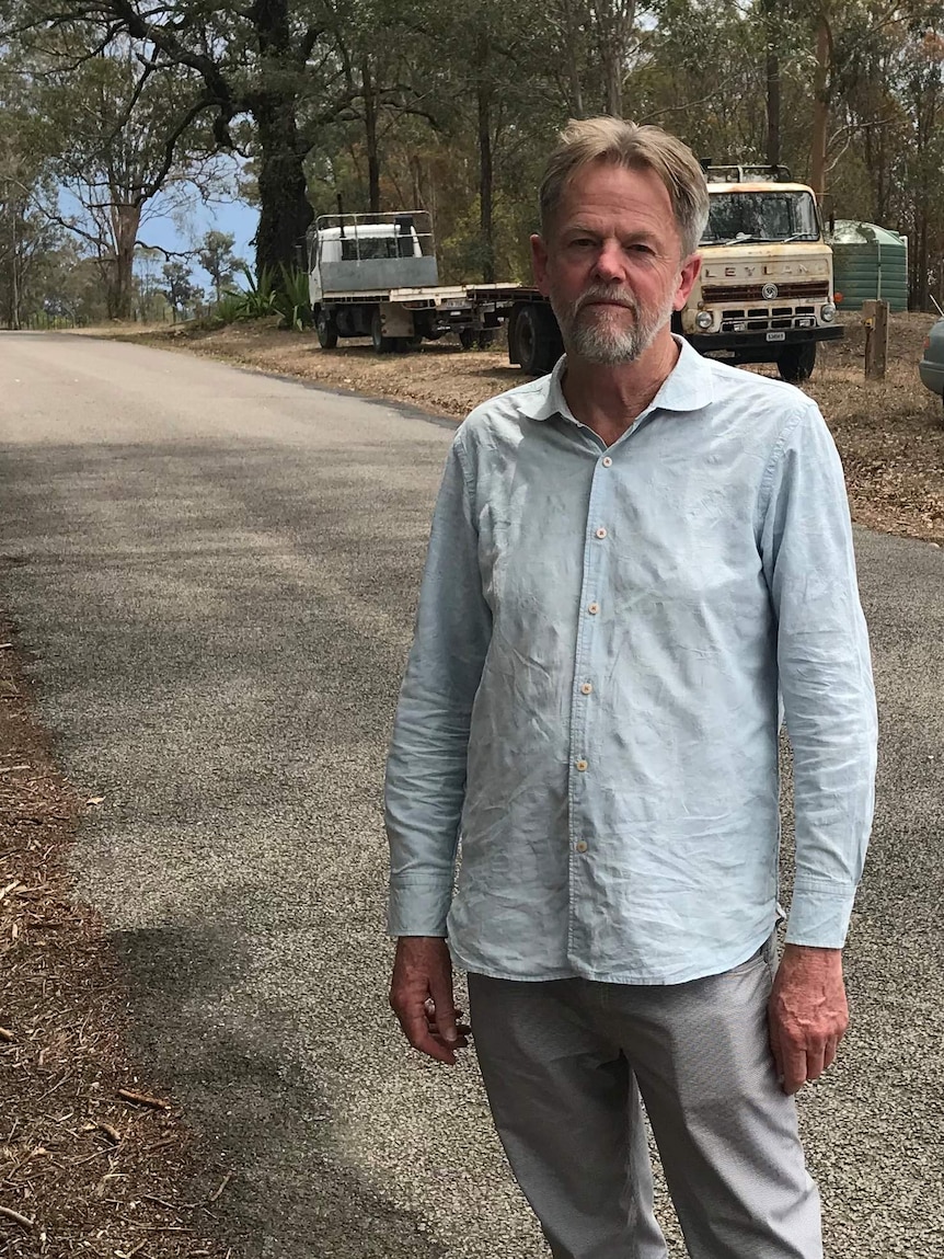 A man stands on a country road with trucks in the background