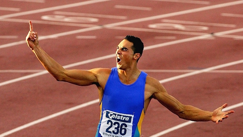A male sprinter in a blue suit points to the sky in excitement at the end of a race
