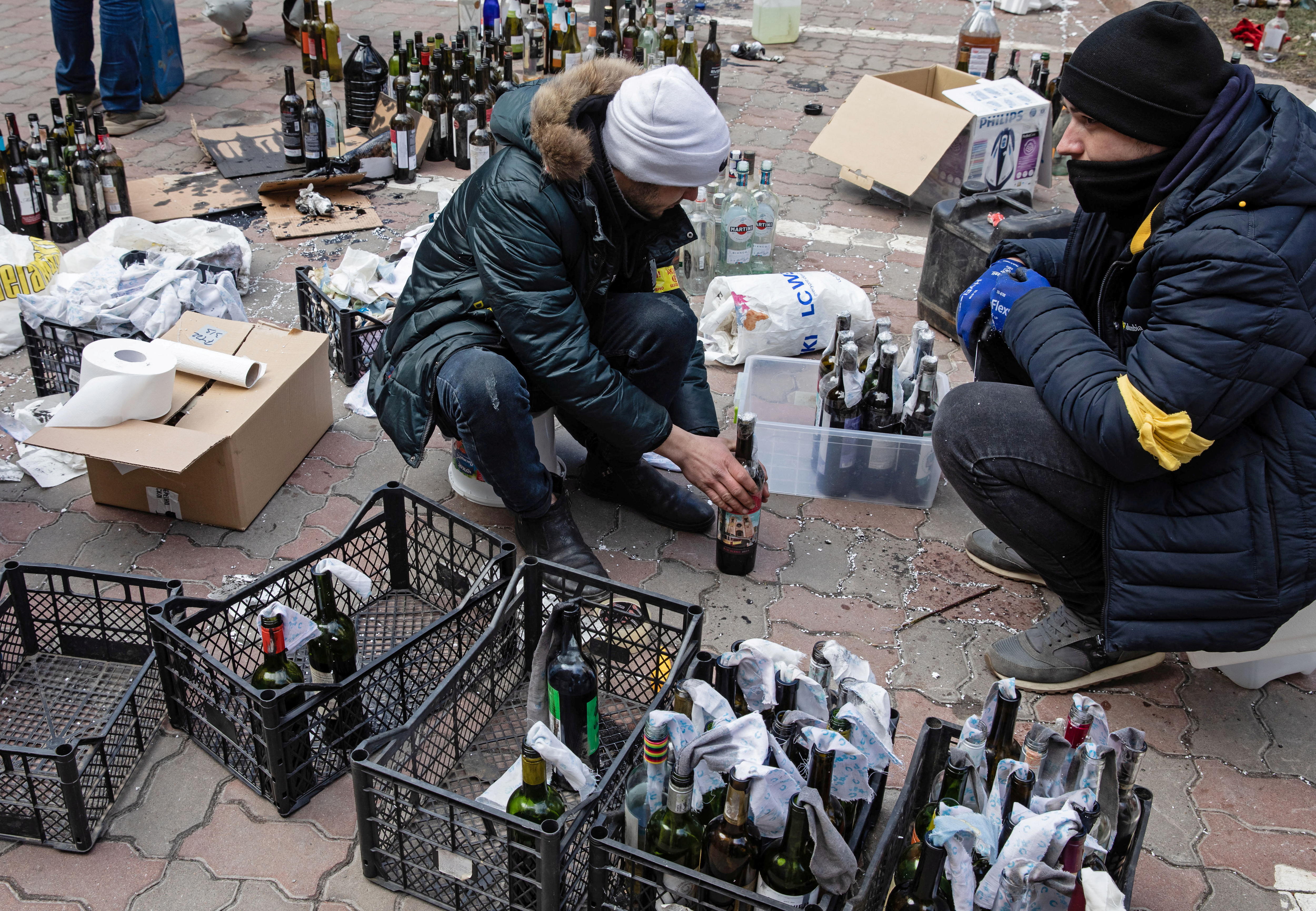 Two men crouched as they prepare molotov cocktails.
