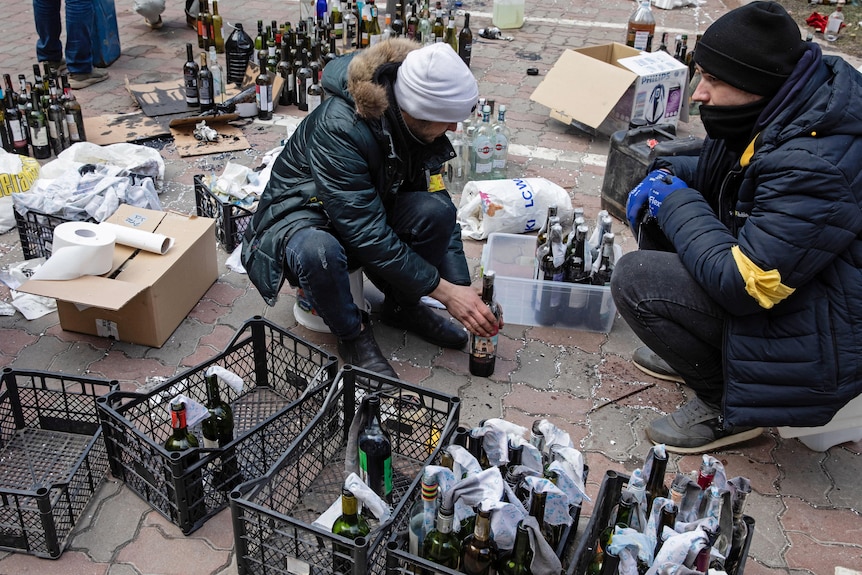 Two men crouched as they prepare molotov cocktails.