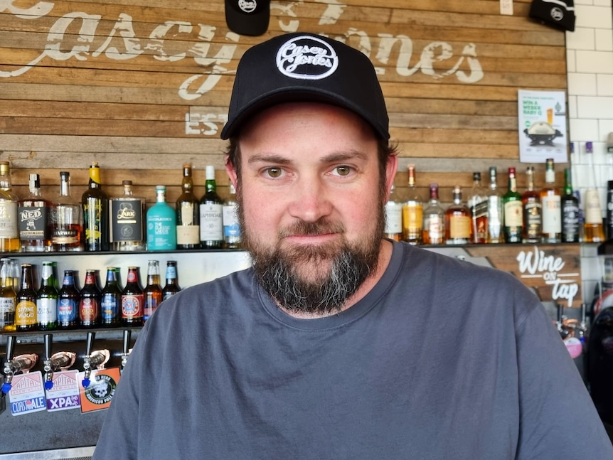 A man in a cap stands in front of a bar.