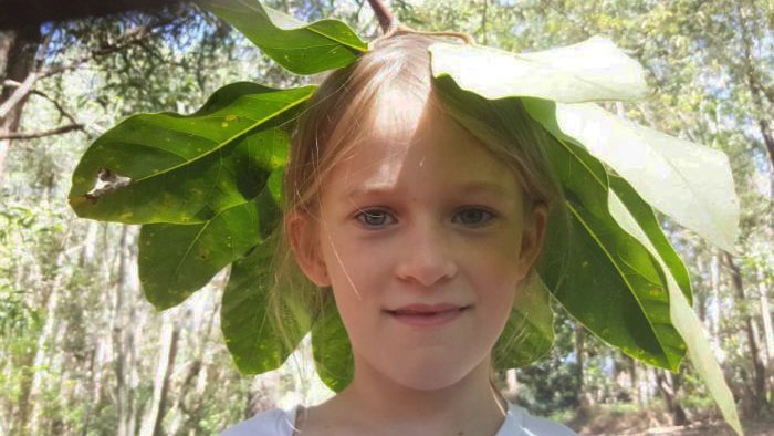 Mayla in nature with an Umbrella Tree frond over her head.