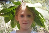 Mayla in nature with an Umbrella Tree frond over her head.