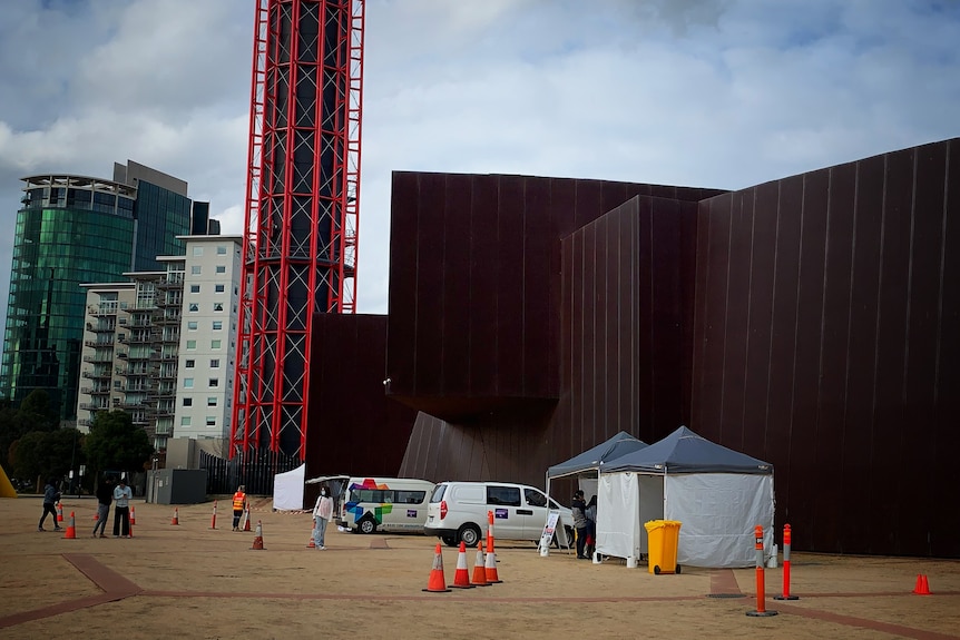 A brown building with tents and people in front at a testing centre.