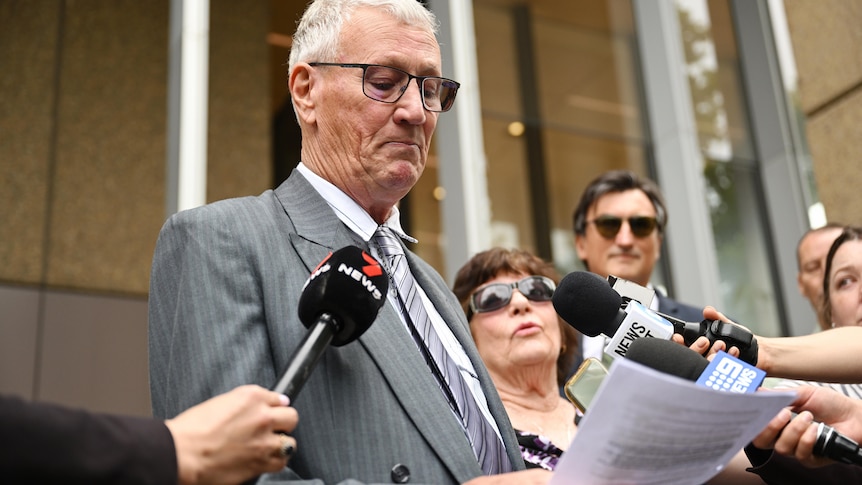 A man wearing glasses addresses reporters