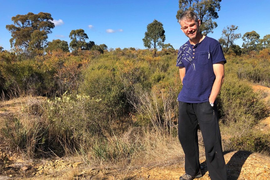 caucasian man wearing casual clothes stands on yellow dry soil, in front of bushland