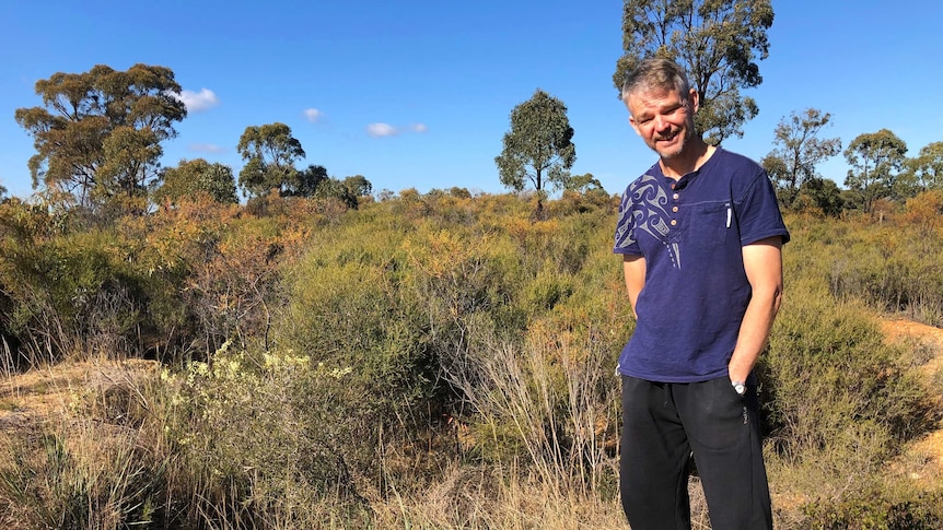 caucasian man wearing casual clothes stands on yellow dry soil, in front of bushland