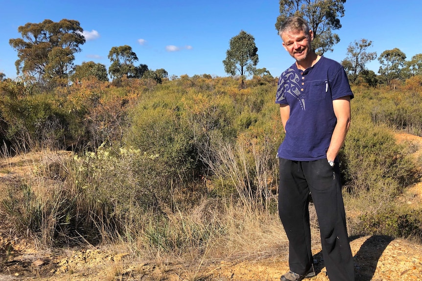 caucasian man wearing casual clothes stands on yellow dry soil, in front of bushland