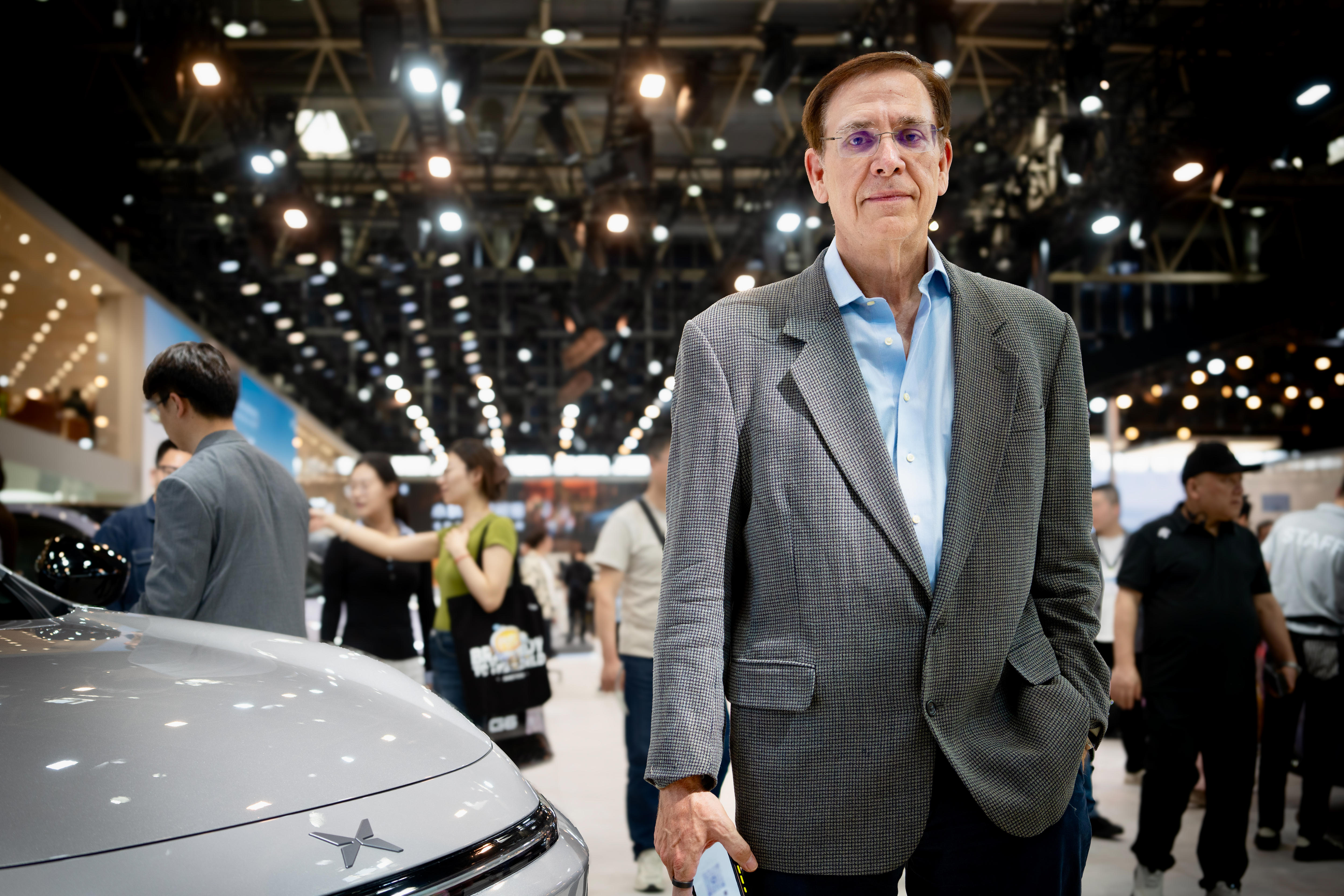 A man in a grey blazer and blue shirt, wearing glasses