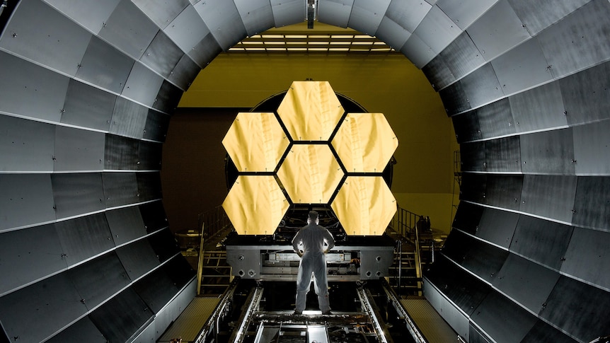 Man stands in front of telescope mirrors 