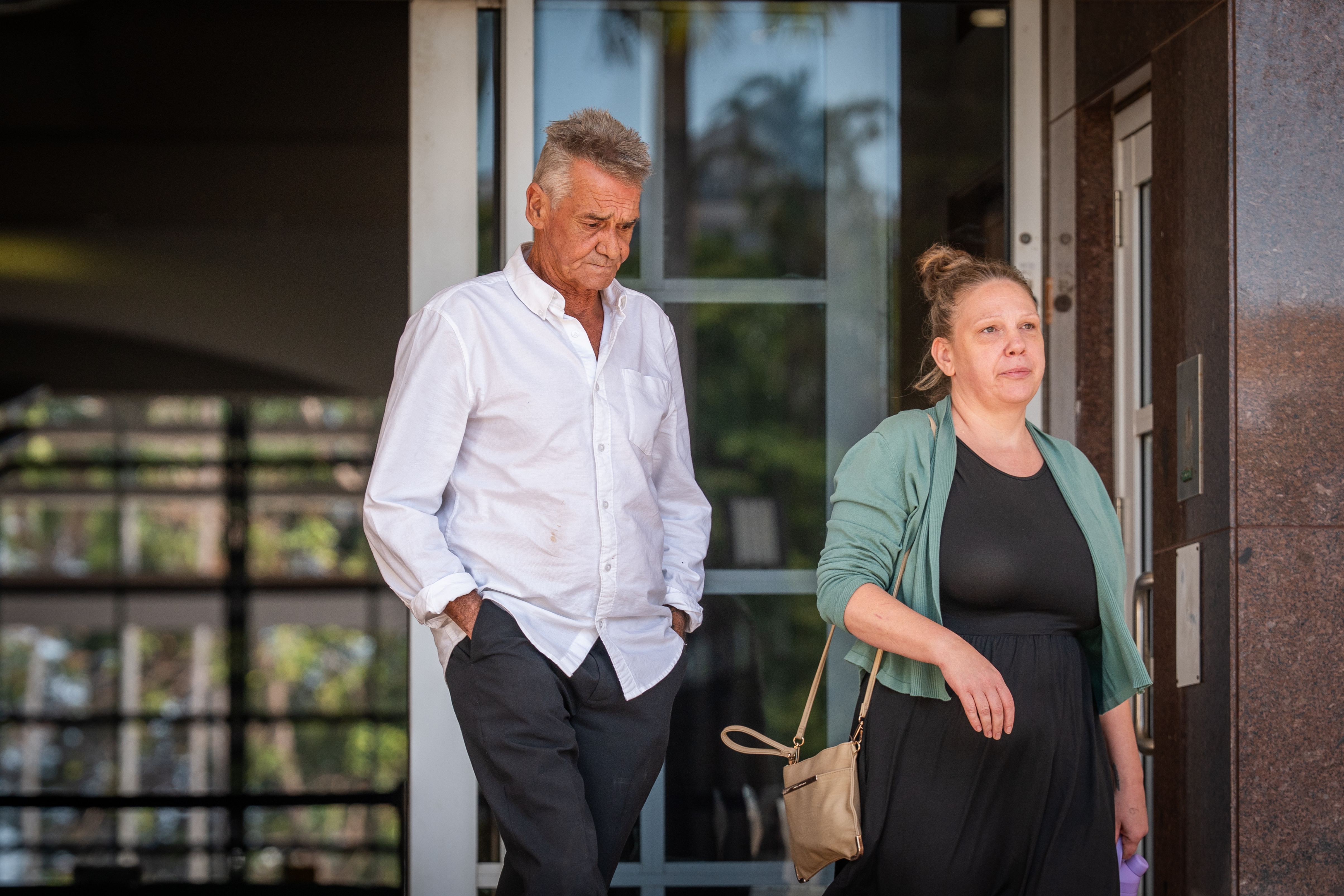 A man with his head bowed and a woman walk out of a court house side-by-side.
