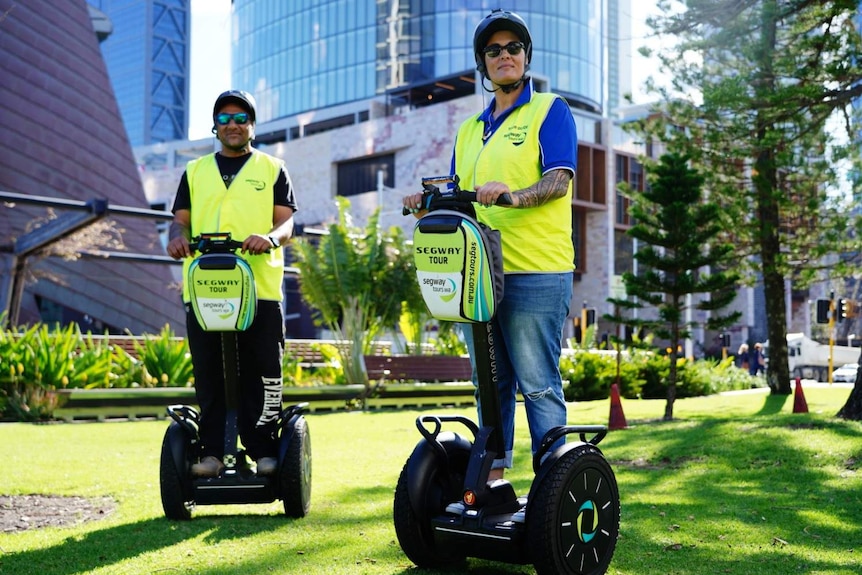 A man and woman in hi-vis shirts and helmets stand stationary on segways.