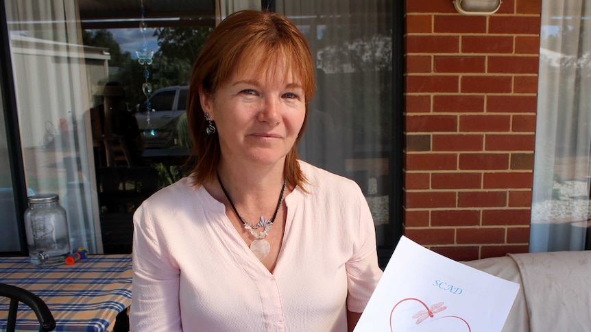 Pamela McKenzie sitting at a table holding a draft copy of her book about SCAD.