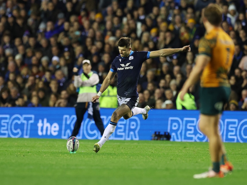 A Scottish rugby union player looks down at the ball as he runs in to kick a penalty during a Test.