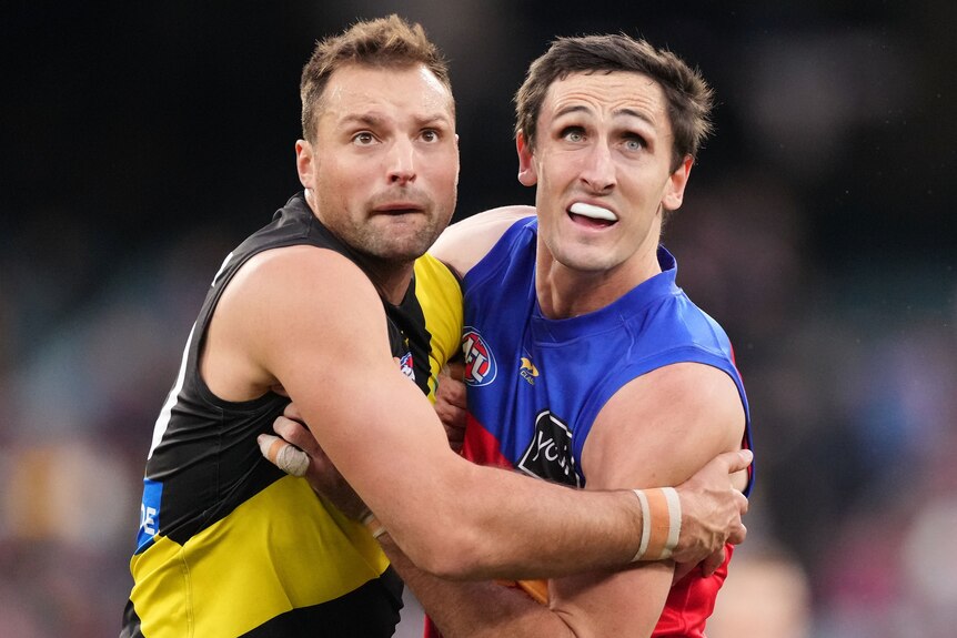 A Richmond AFL player pushes against a Brisbane opponent as they prepare to challenge for the ball.