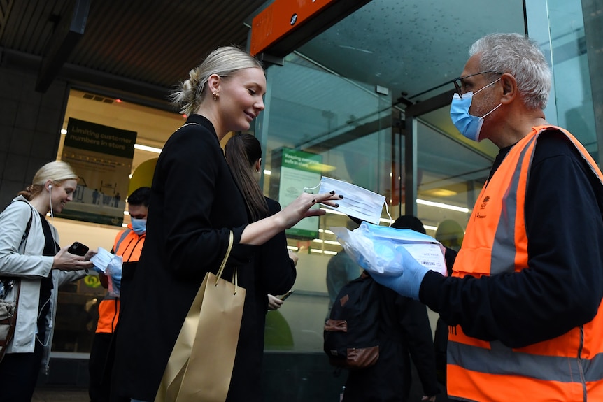 a woman reaches her hand out to get a mask from a man with  covered face