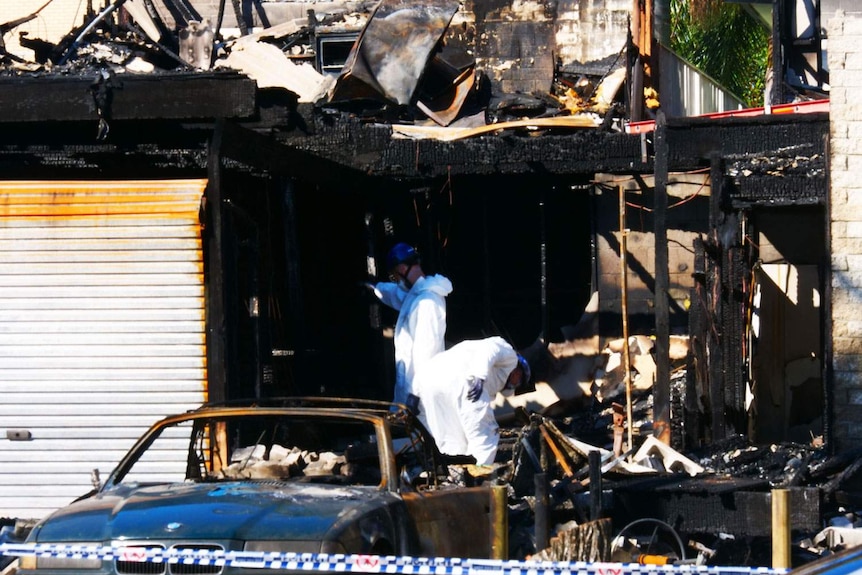 Two forensic officers investigate the burnt-out unit complex.