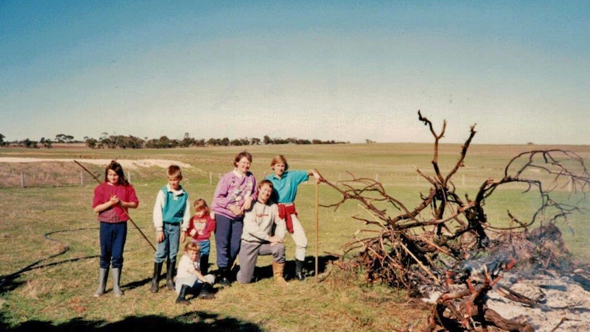 Old photo of a family posing in a paddock next to smouldering tree branches on the ground