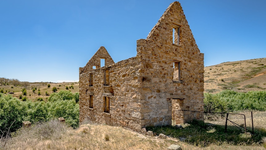 An old stone building with no roof in a field, surrounded by grass and trees.