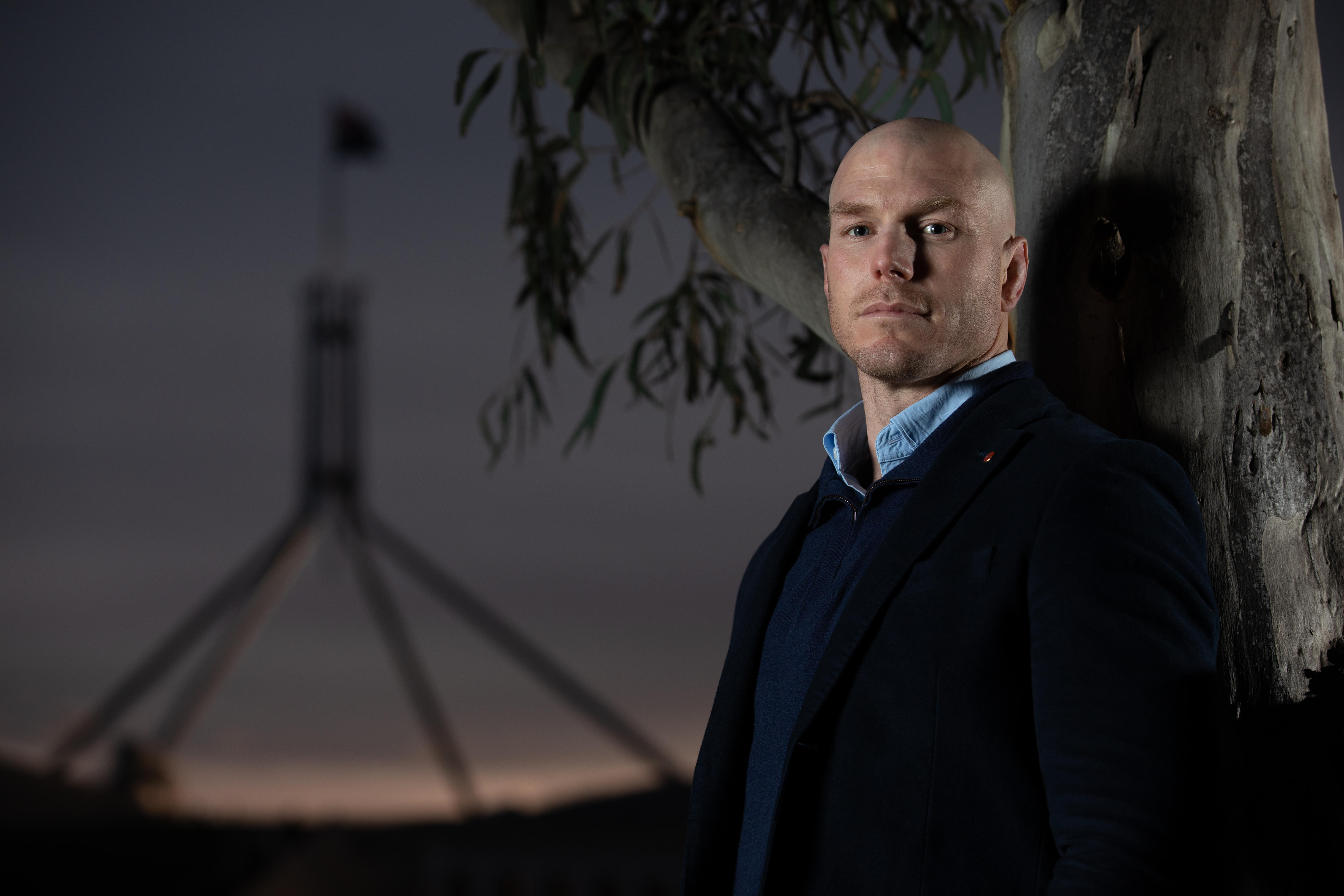 David Pocock looks out at distance in portrait taken in front of sunset at parliament house