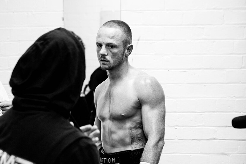 A man wearing boxing gloves looking at a man in a black hoodie.