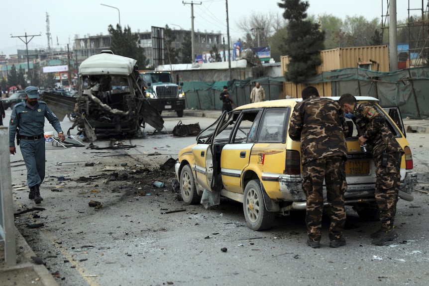 Several soldiers look into the back of a bombed out car