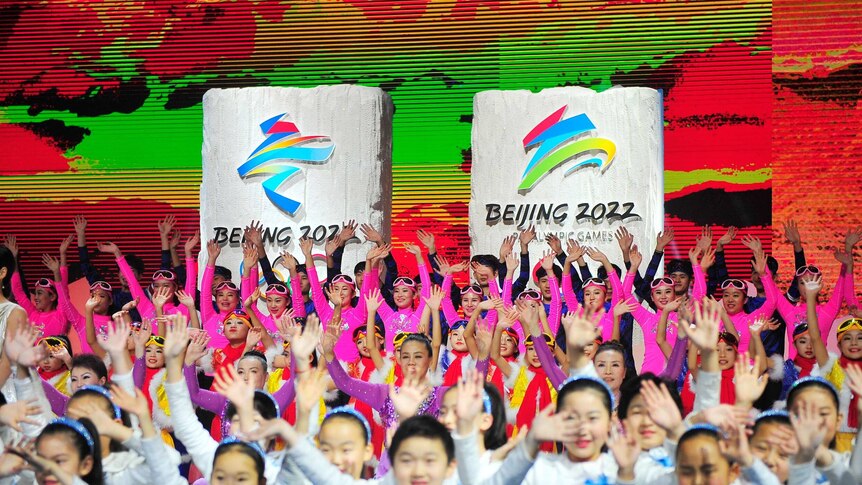 People in colourful outfits stand in front of banners that read Beijing 2022.