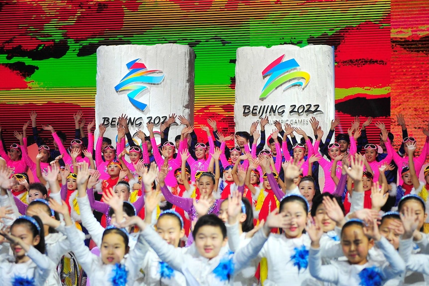 People in colourful outfits stand in front of banners that read Beijing 2022.