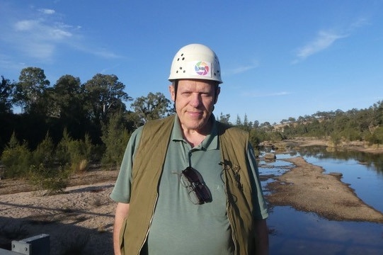 A man in a hard hat near creek stares down lens of camera