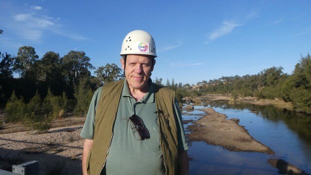 A man in a hard hat near creek stares down lens of camera