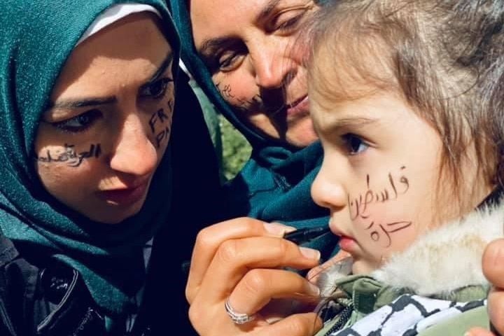 Aseel writing in Arabic on a child's face during the protest.