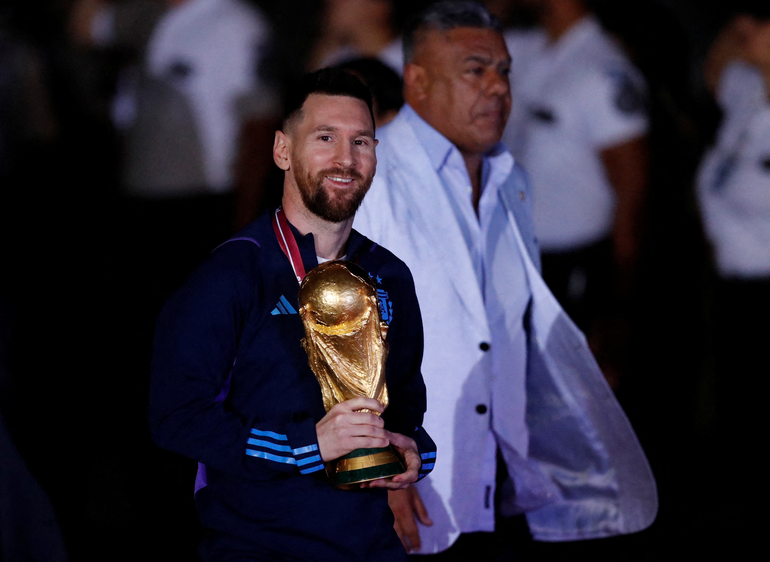 Lionel Messi holds the gold world cup trophy while smiling towards the camera. 