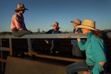 Woman sitting on a cattle rail speaking with three girls. 