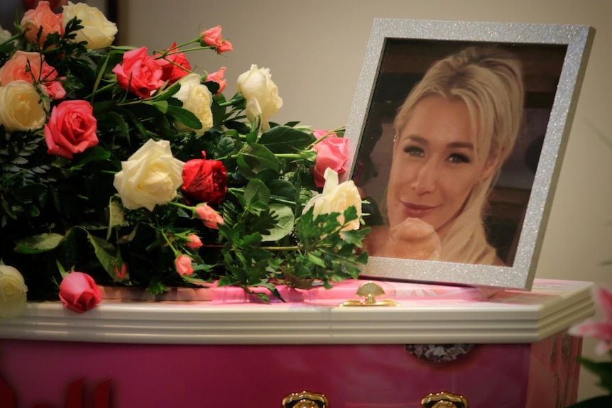 La photographie d'une jeune femme, Ellie Price, se trouve au sommet d'un cercueil rose à côté d'un bouquet de roses blanches et roses.