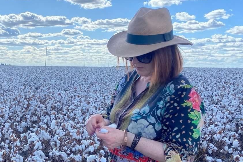 a woman in hat and sunnies stands in a cotton field. 