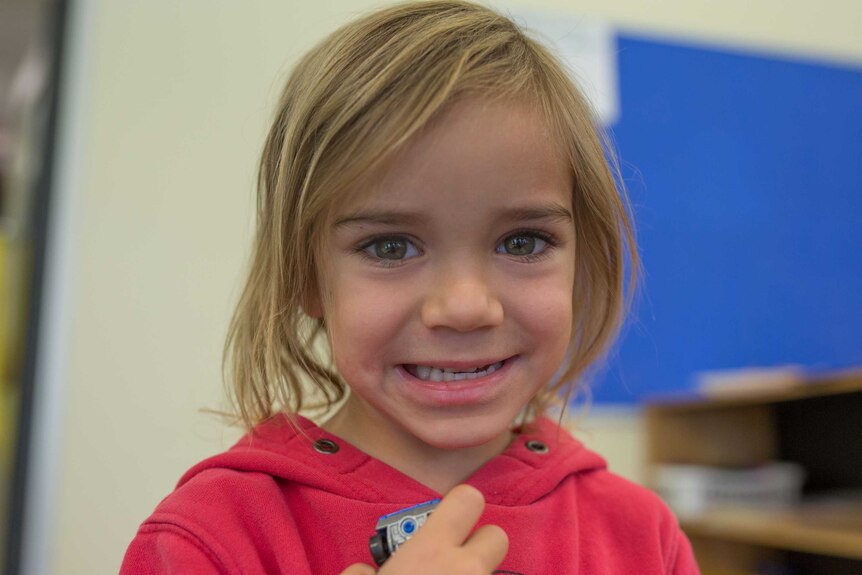 A girl at Lulla's grins as she holds a toy car.