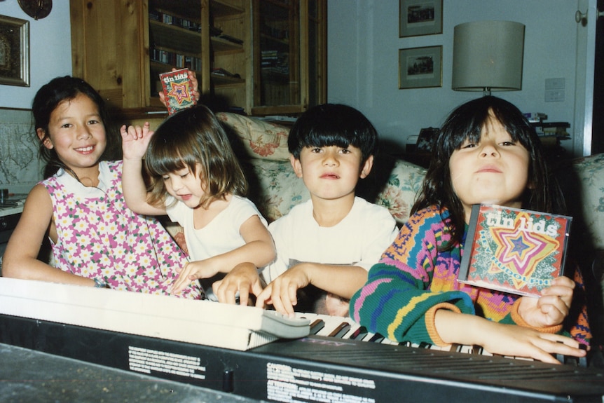 All four siblings at a keyboard, one holds a CD that says 'Tin Lids'.