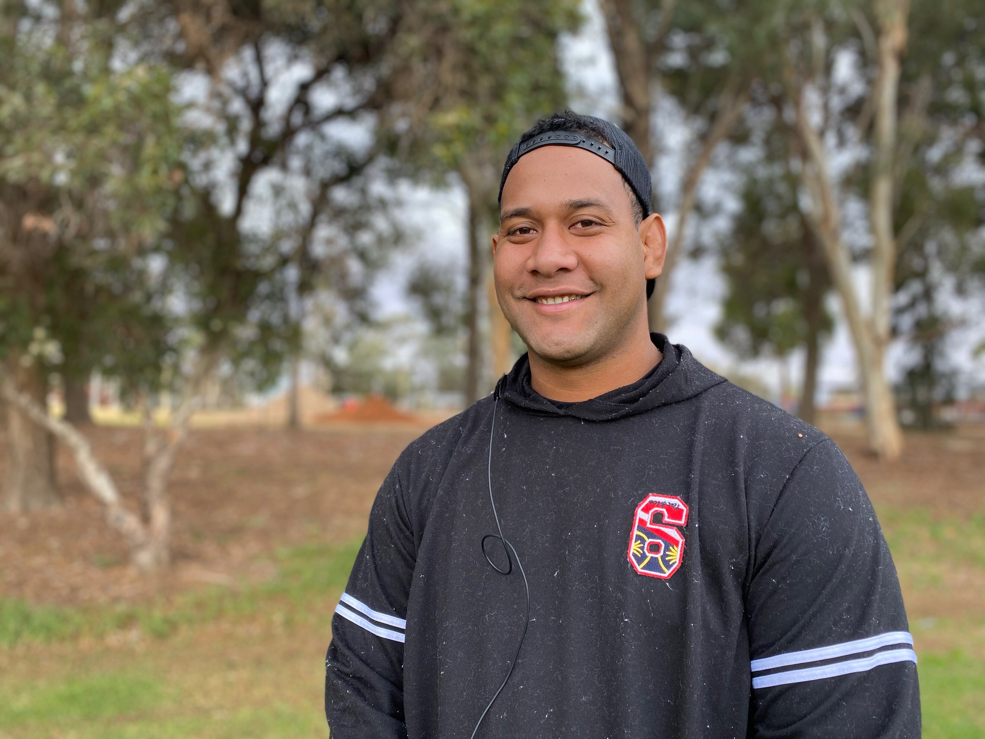 Pacific Islander man wearing a dark jumper with the number 6 on it and a cap turned backwards
