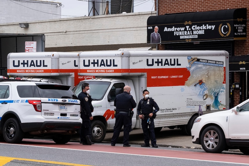 Police officers wearing face masks stand next to two UHAUL trucks on the side of a road, outside Andrew T. Cleckley Funeral Home