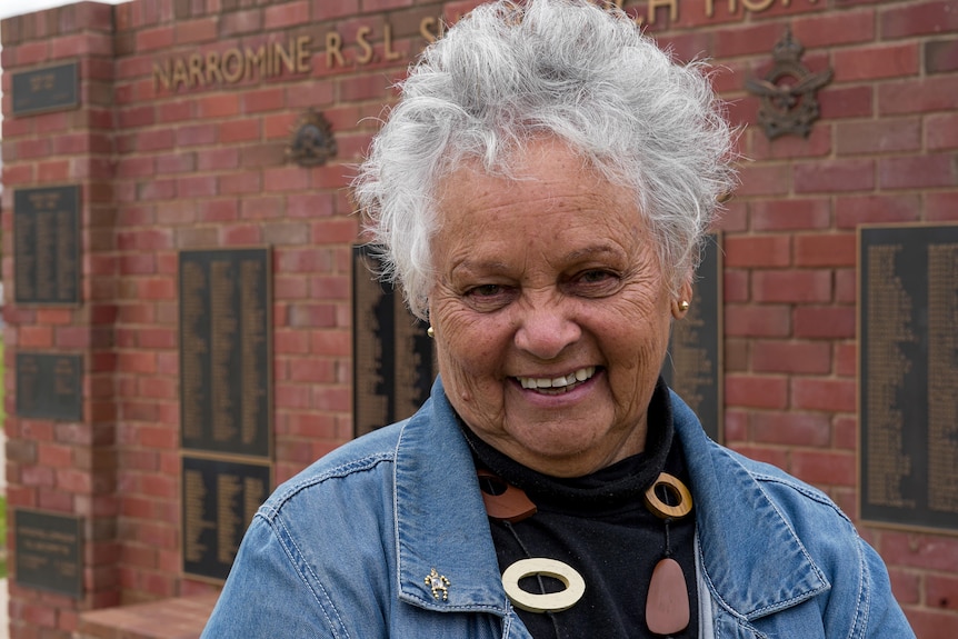 A woman in a denim jacket stands in front of a wall of memorial to Australian soldiers