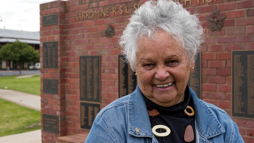 A woman in a denim jacket stands in front of a wall of memorial to Australian soldiers