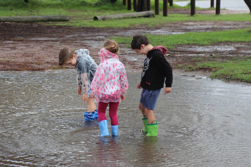 Children wearing gumboots play in a puddle.
