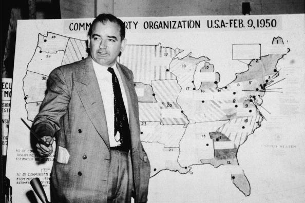 Joseph McCarthy stands gesturing at a shaded map of America