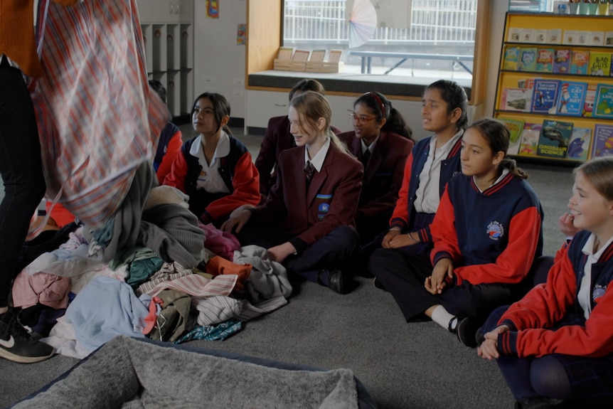 Students watch as a teacher empties bags of clothing onto the floor.